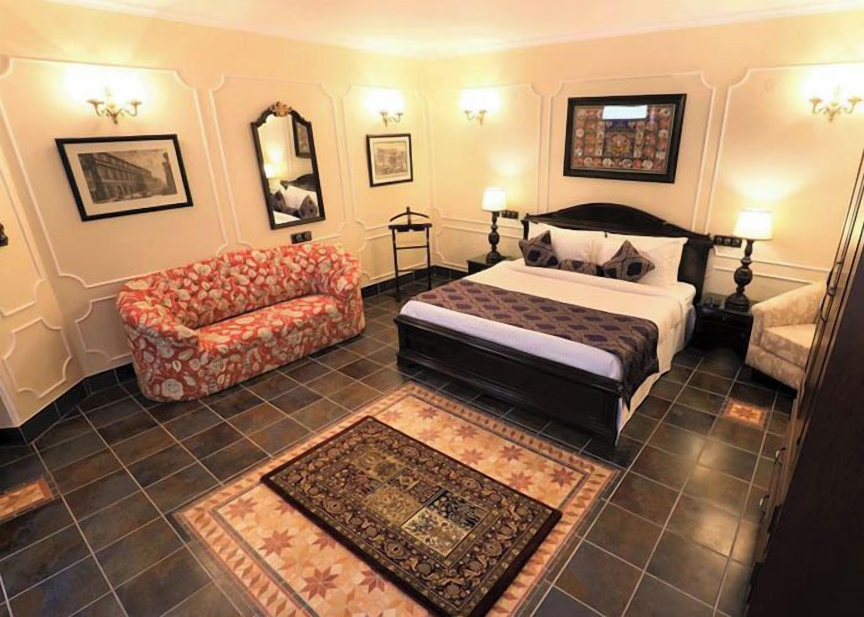A bedroom with a bed, a sofa, a rug, and wall-mounted lamps.