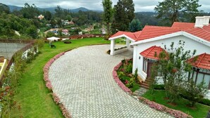 A white building with a red roof, surrounded by a landscaped garden and a paved driveway. - Rock Ooty Heritage Villa (Ootacamund)