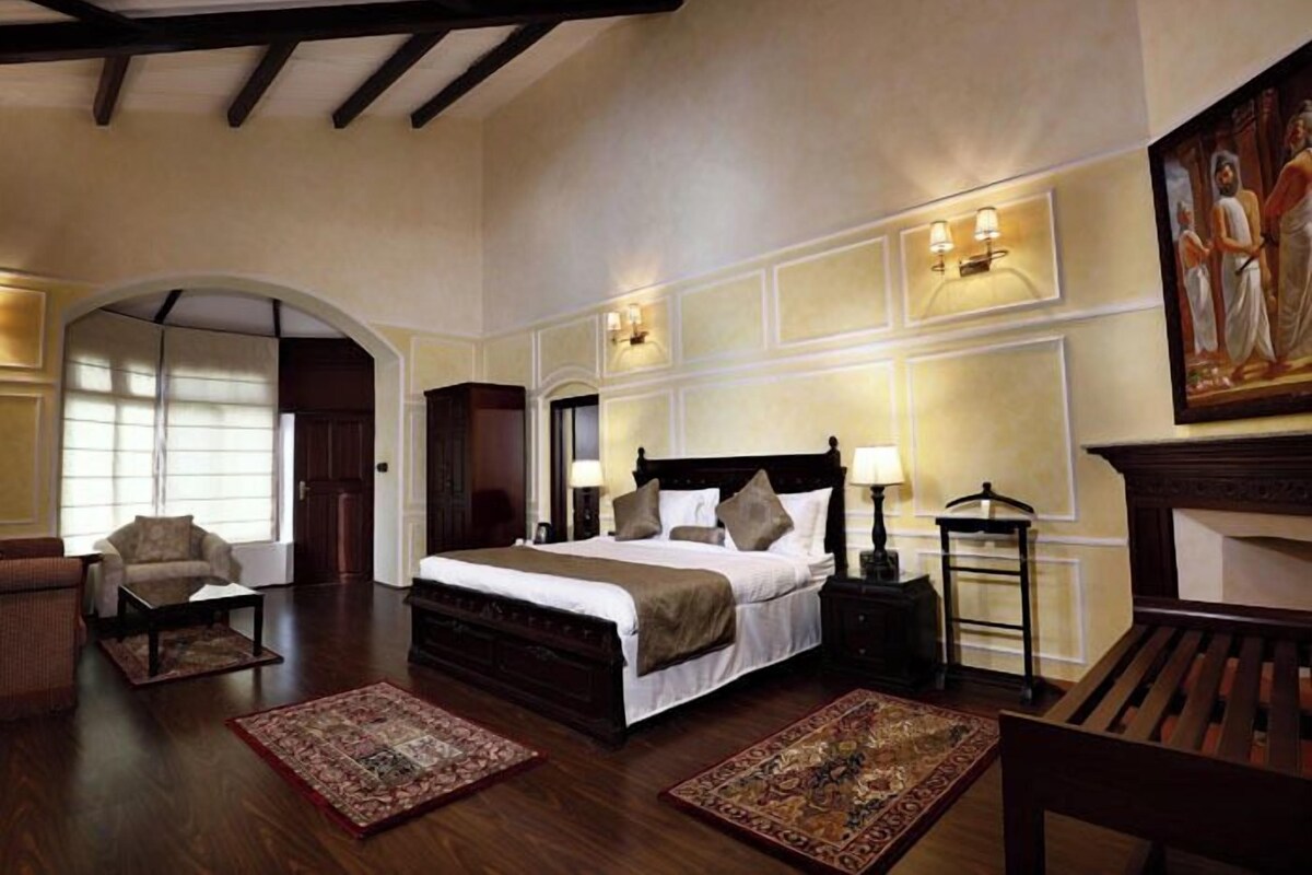 A spacious bedroom with a large bed, two bedside tables with lamps, a chair, and a fireplace.