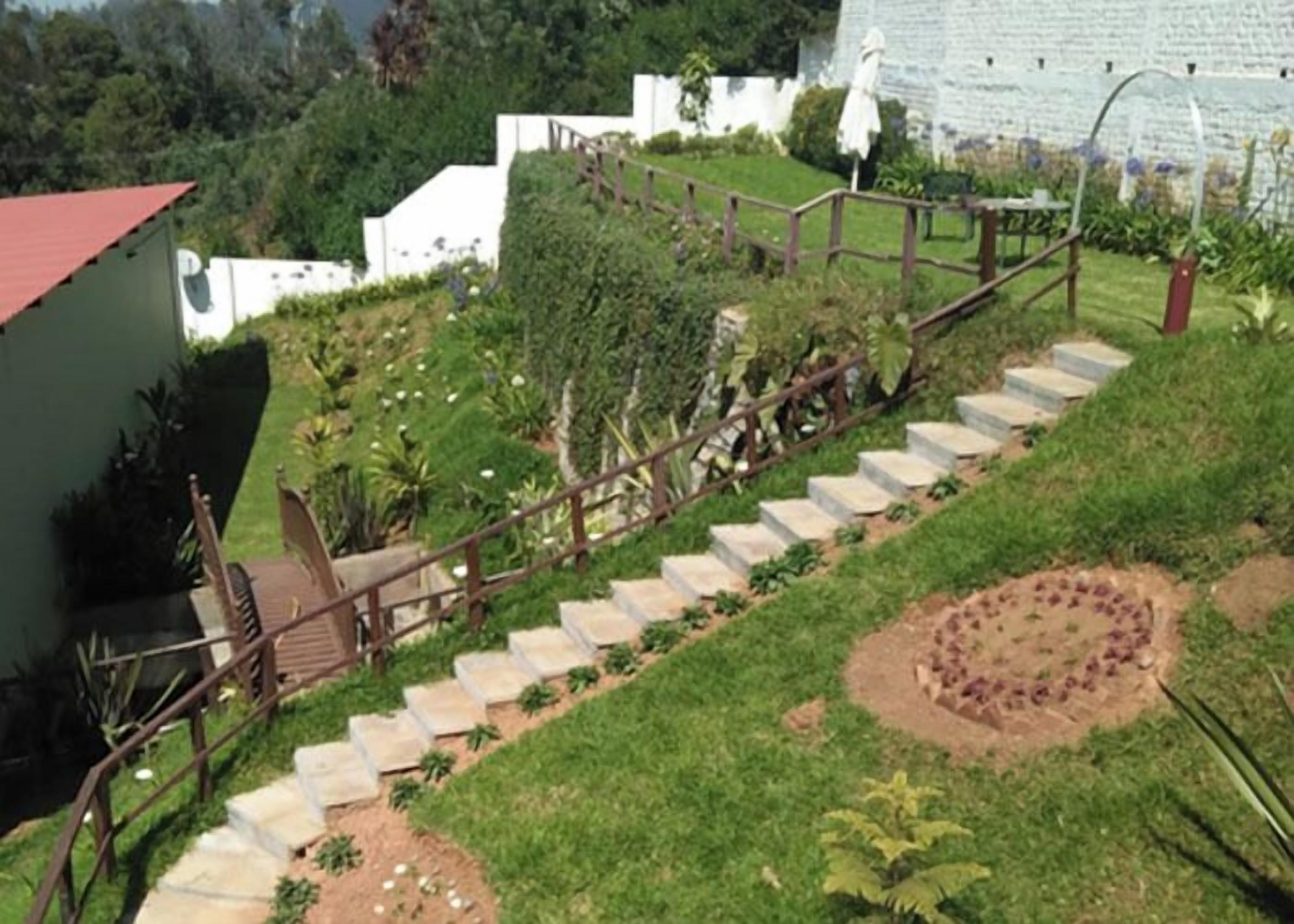 A set of outdoor stairs leading up to a building with a red roof, surrounded by greenery and a garden area.