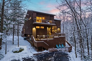 A multi-level wooden cabin with a deck, surrounded by snow-covered trees. - Waterfall Views! Hot Tub, Game Room, Dog Friendly (Bushkill)