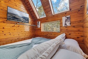 A cozy wooden cabin room with a bed, a window, and a painting of a wolf. - Waterfall Views! Hot Tub, Game Room, Dog Friendly (Bushkill)