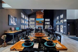 A dining area with a long table set for a meal, surrounded by chairs, with a fireplace and a television in the background. - Waterfall Views! Hot Tub, Game Room, Dog Friendly (Bushkill)