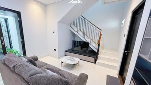 A modern living room with a grey sofa, a coffee table, and a staircase with a glass railing. - Aruna Kalasan (Depok)