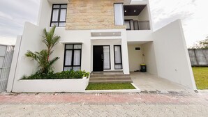 A modern two-story house with a stone facade, white exterior, and a balcony. - Aruna Kalasan (Depok)