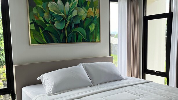 A modern bedroom with a large bed, a painting of flowers on the wall, and a window with curtains. - Aruna Kalasan (Depok)