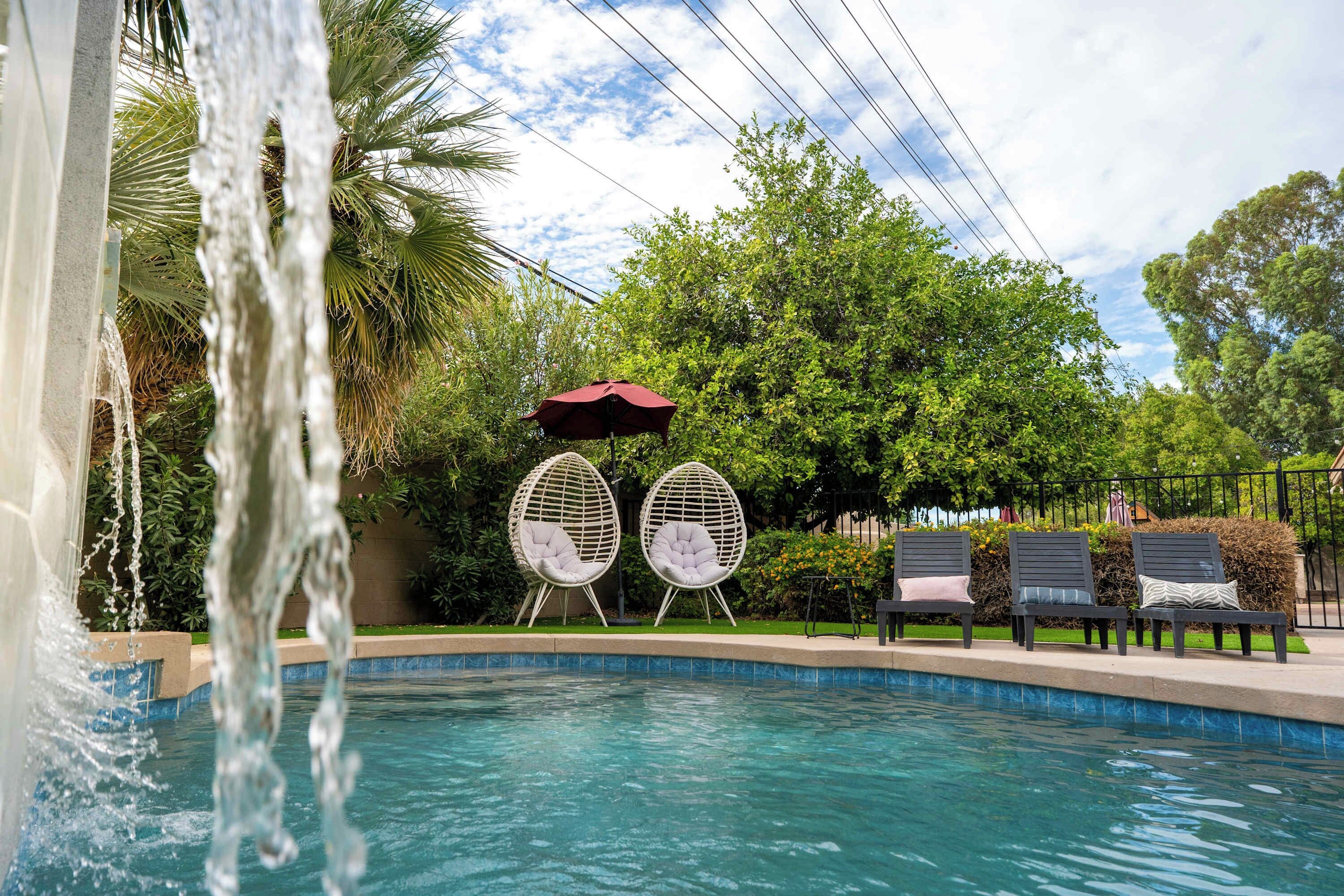 A swimming pool with two white egg-shaped chairs and a red umbrella.