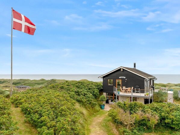 Una casa costera con balcón que da al mar, rodeada de exuberante vegetación.
