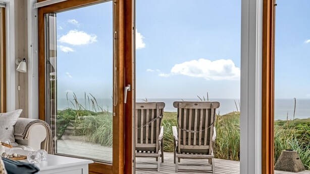 Habitación con vista al mar, que incluye una terraza de madera, dos sillas de madera, un sofá blanco y cestos de mimbre.