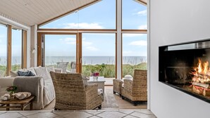 Una habitación amplia con ventanas grandes, chimenea y vistas al mar.