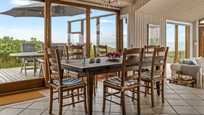 Un comedor con una mesa grande y sillas, una araña y vistas al mar.