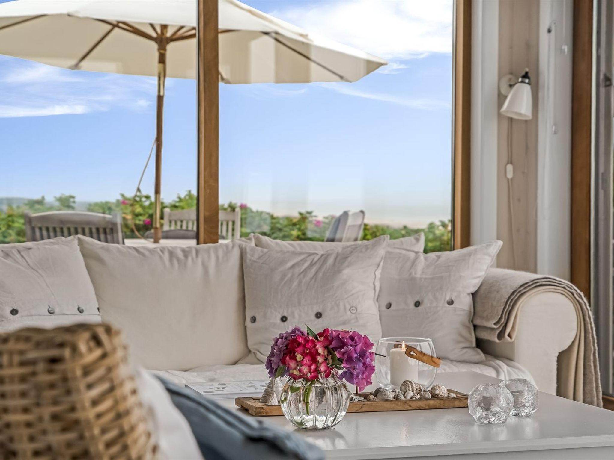 Ein gemütlicher Sitzbereich im Freien mit einer Couch, einem Tisch mit Kerze, Blumen und Blick auf die Landschaft.
