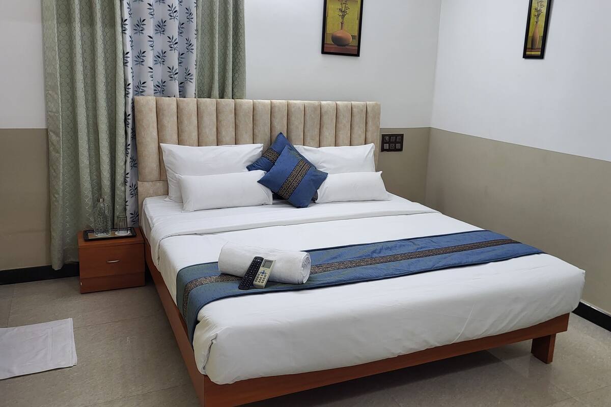 A neatly made bed with a beige headboard, white bedding, and a blue and gold throw blanket.
