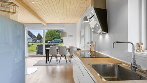 Eine moderne Küche mit Holzboden, einem großen Fenster und einem Essbereich mit Stühlen und Tisch.