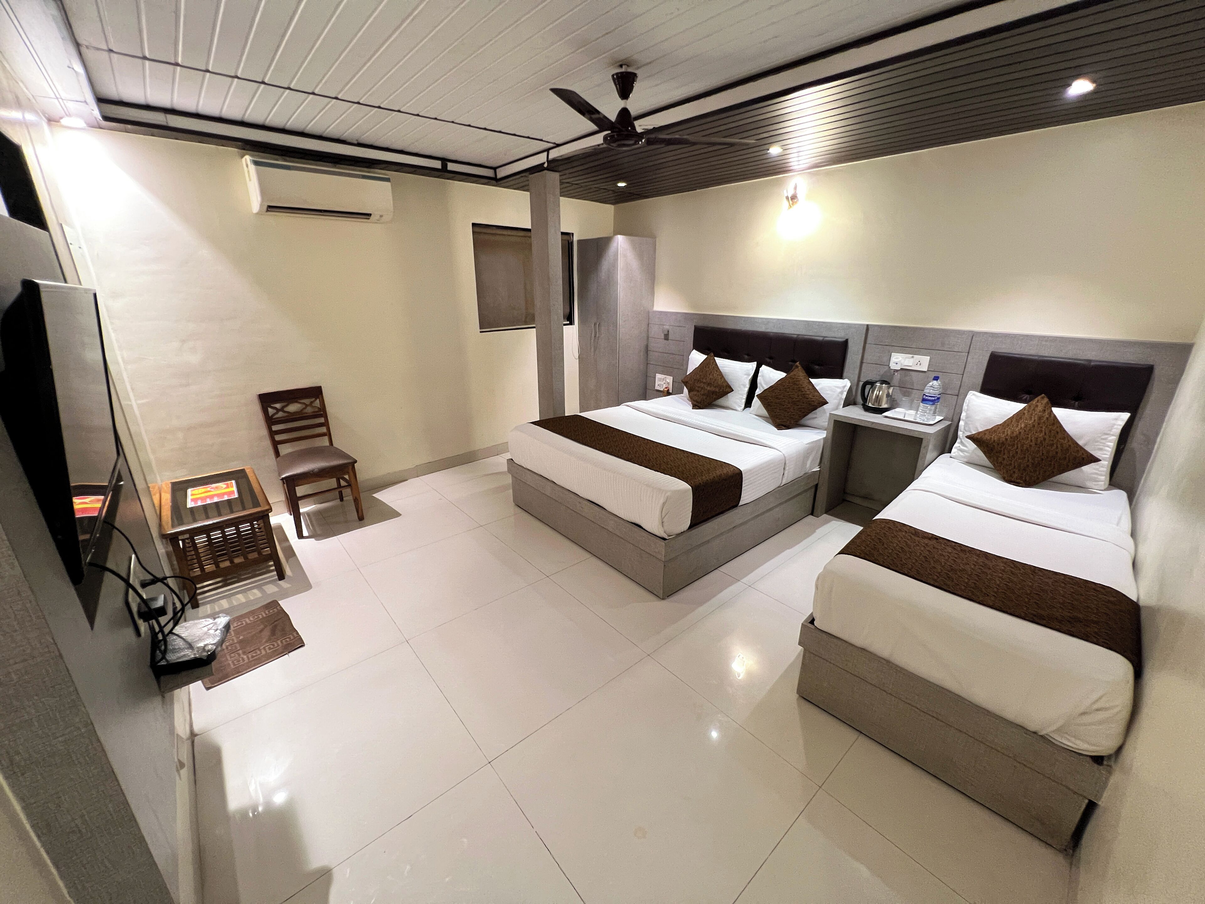 A hotel room with two beds, a TV, a chair, and a small table.