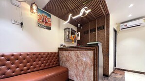 A reception area with a brown leather sofa, marble reception desk, and a ceiling with wooden paneling and recessed lighting. - New Hotel Prince Palace (Mumbai)