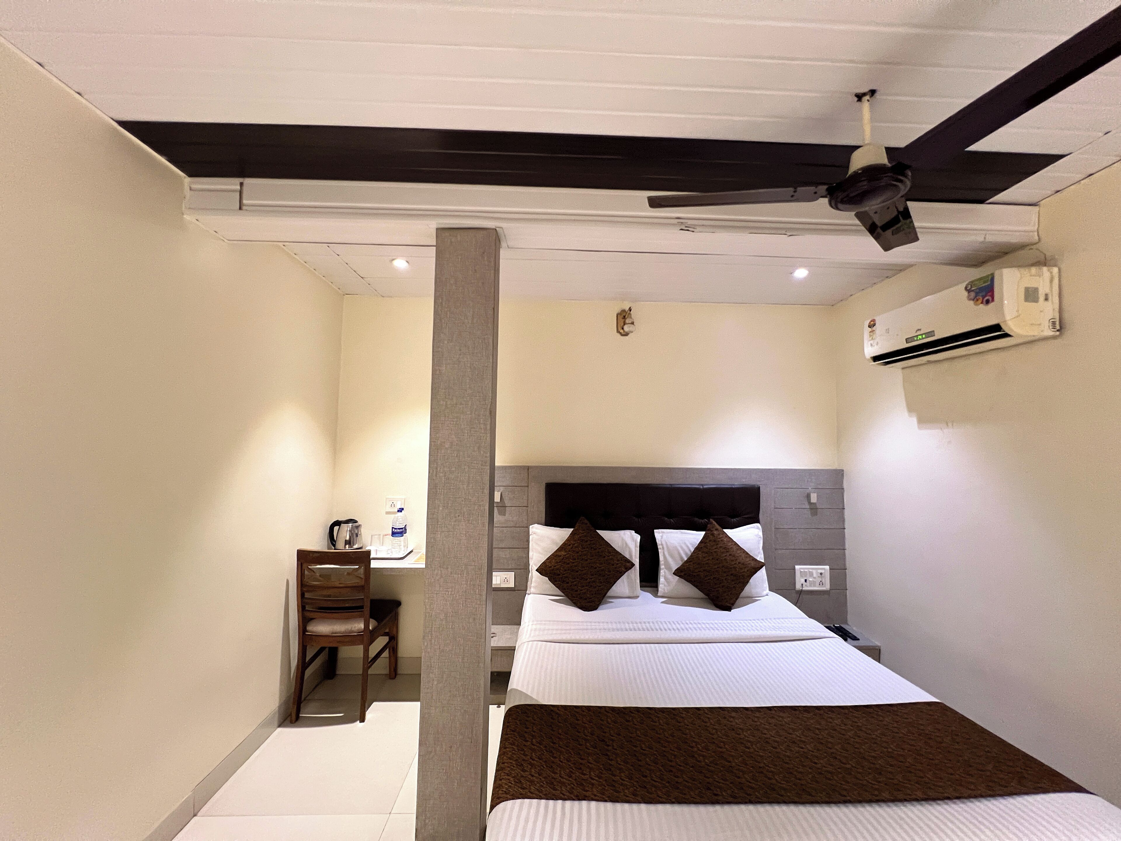 A hotel room with a bed, a desk, a chair, a ceiling fan, and an air conditioning unit.