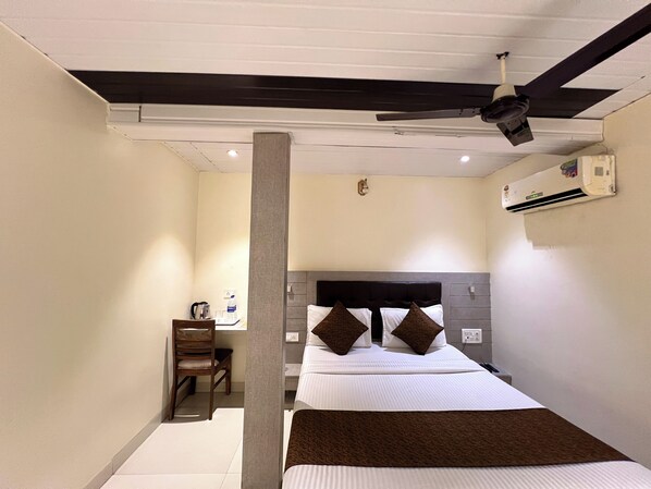 Une chambre d’hôtel équipée d’un lit, d’un bureau, d’une chaise, d’un ventilateur de plafond et d’un appareil de climatisation.