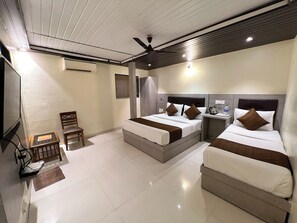 Quarto de hotel com duas camas, uma mesa, uma cadeira e um ventilador de teto.
