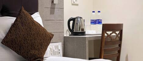 Quarto de hotel com cama, escrivaninha, cadeira, chaleira e duas garrafas de água.