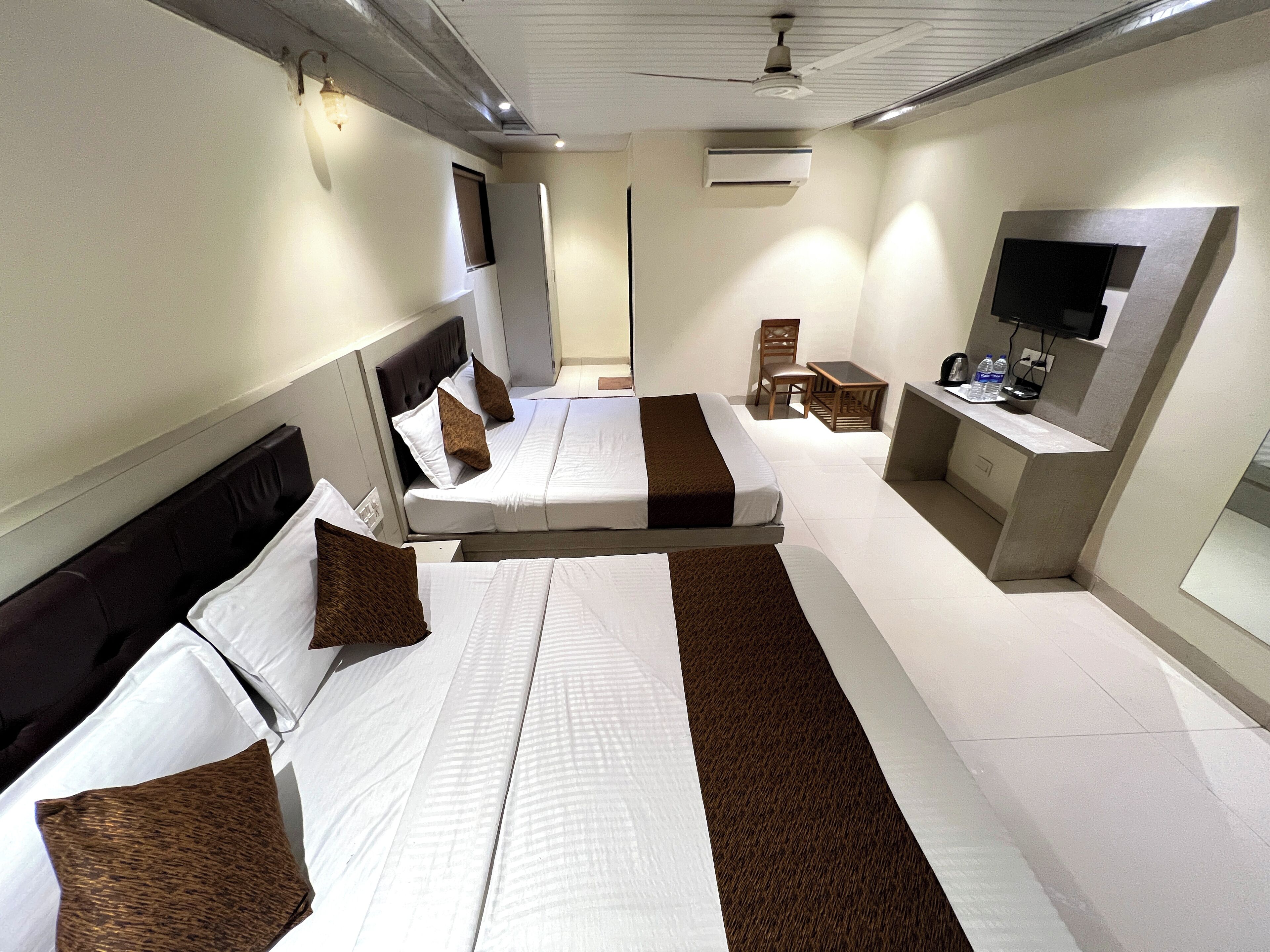 Une chambre d’hôtel avec deux lits, un bureau, une chaise, une télévision et un appareil de climatisation.