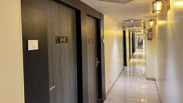 A hotel hallway with dark wooden doors, numbered room signs, and wall-mounted light fixtures. - New Hotel Prince Palace (Mumbai)