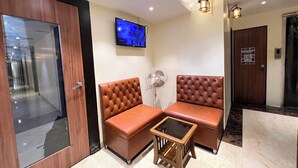 A lobby with a wooden door, two leather sofas, a small wooden table, a standing fan, and a mounted TV. - New Hotel Prince Palace (Mumbai)