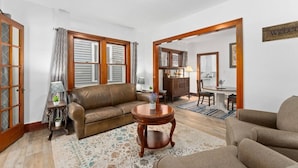 A spacious living room with a brown leather sofa, a wooden coffee table, and a dining area with a table and chairs. - Charming Centrally Located Sunroom/Fireplace (Sioux Falls)