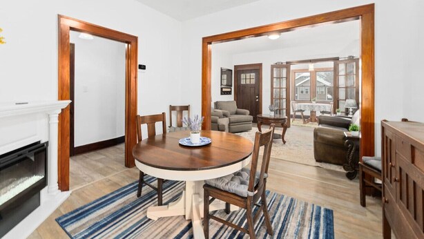 A dining area with a round table, chairs, and a fireplace. There is a living room with a sofa and a dining table visible through an open door. - Charming Centrally Located Sunroom/Fireplace (Sioux Falls)