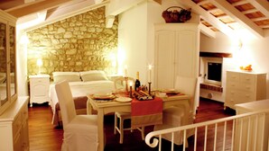 A cozy bedroom with a stone wall, a bed, a dining table with candles, and a television. - Residenza dei TOLOMEI Confort Relax Centro Storico  (Polcenigo)