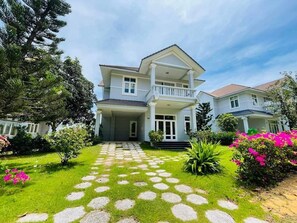 A two-story house with a balcony, a well-maintained lawn, and a stone pathway leading to the entrance. - Deluxe Soan Villa - Sealinks Mui Ne (Phan Thiet)