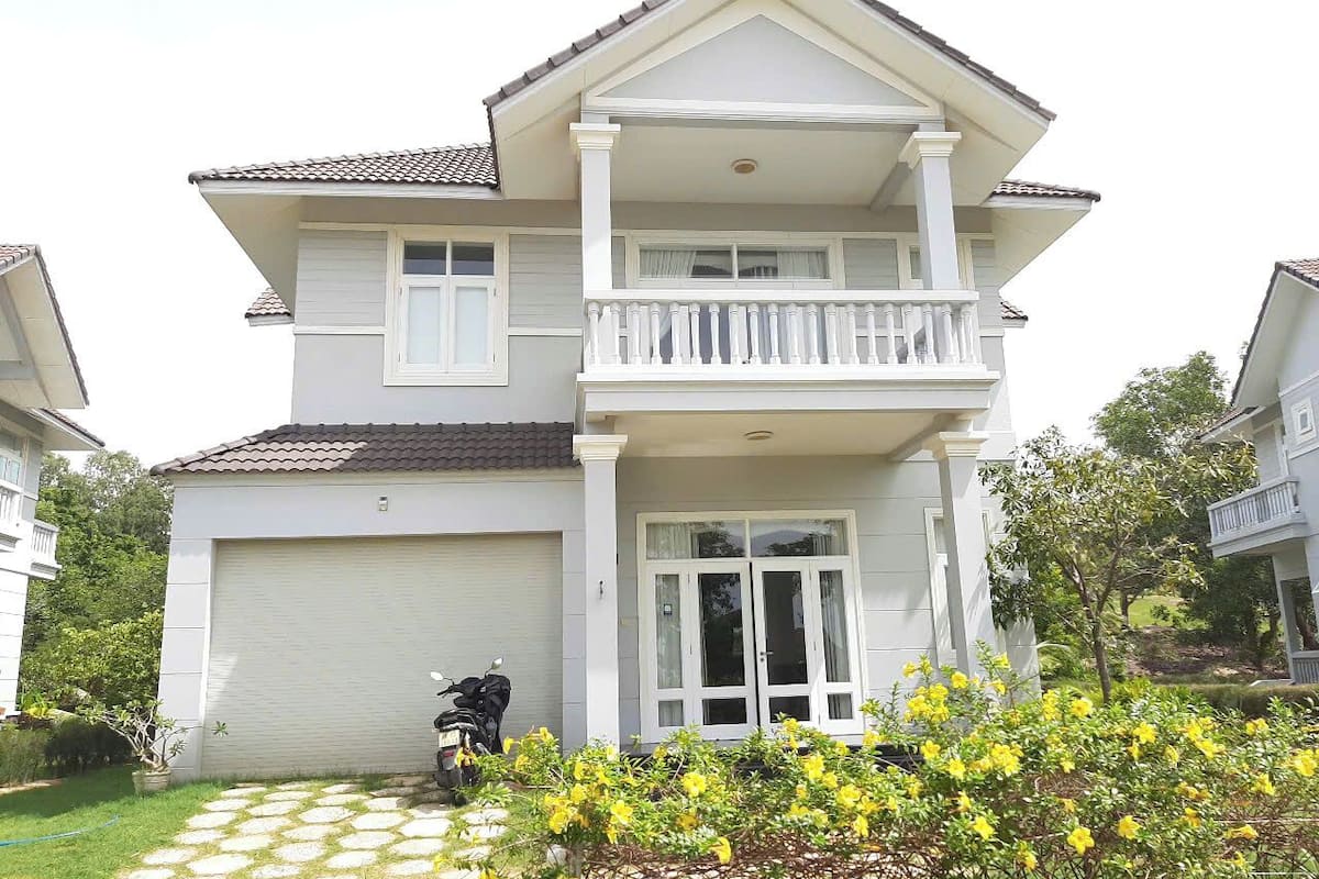 A two-story house with a garage, a balcony, and a garden with yellow flowers.