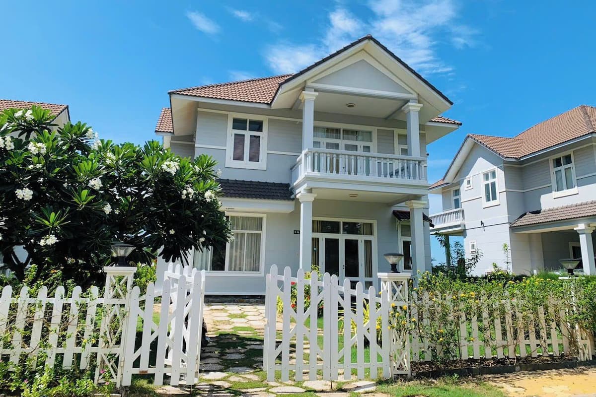 A two-story house with a balcony, a white picket fence, and a well-maintained garden.