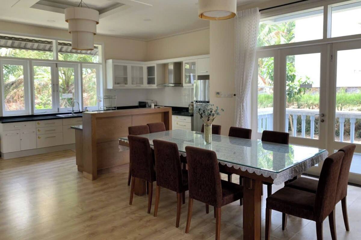 A spacious kitchen with a central island, large windows, and a dining area with a glass table.