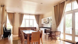 Un vaste espace dédié à la salle à manger, avec une table et des chaises en bois, un piano, et une cuisine en arrière-plan.