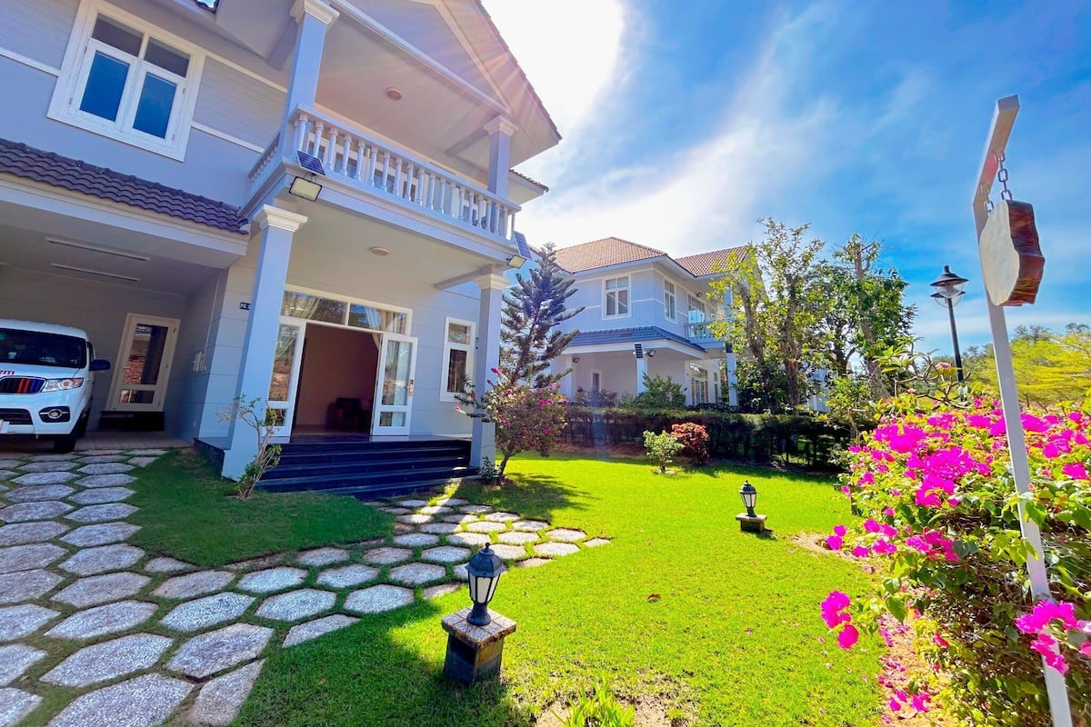 A two-story house with a covered porch, a car parked in the driveway, and a well-maintained garden with flowering plants.