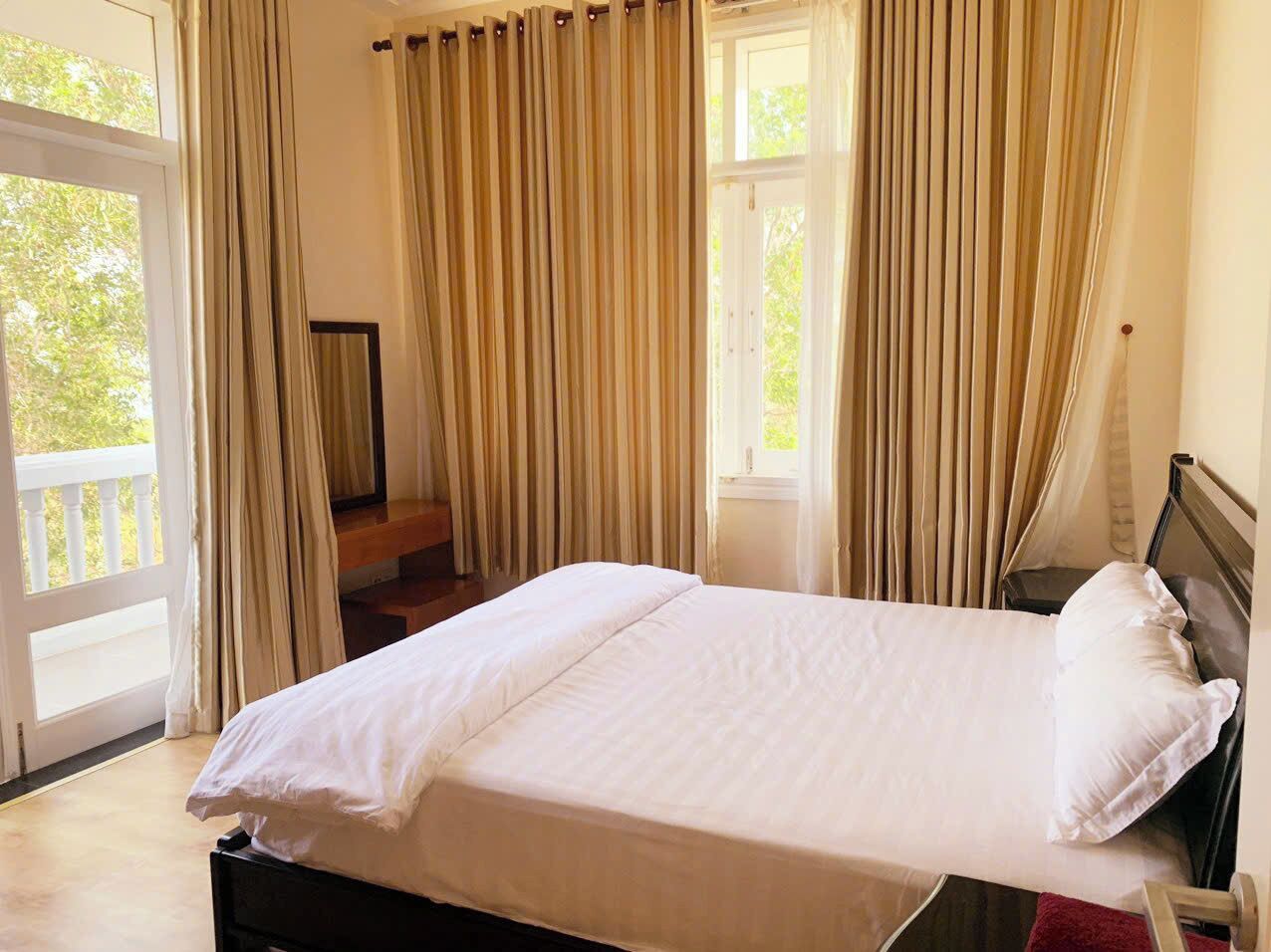 A large bed with white linens in a room with a balcony and curtains.