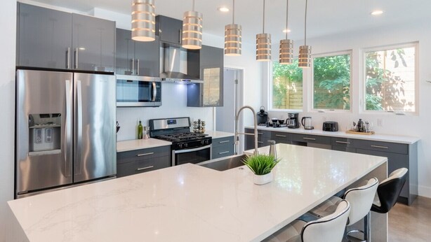 Una cocina moderna con electrodomésticos de acero inoxidable, una isla grande, luces colgantes y vistas al exterior.