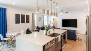 Una cocina moderna con una isla central, electrodomésticos de acero inoxidable, iluminación colgante y un televisor de pantalla plana montado en la pared.