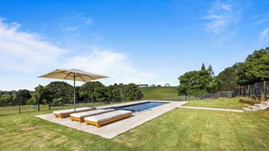 A swimming pool with lounge chairs and an umbrella, surrounded by a well-maintained lawn and trees.
