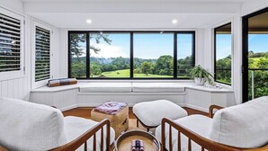 A conservatory with a view of a green landscape, furnished with two chairs and a small table.