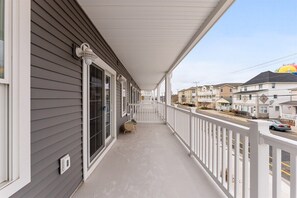 A covered porch with a white railing, a small table, and a window with a view of neighboring houses. - New 3BR Condo with Rooftop Walk to Beach Boardwalk (Wildwood)