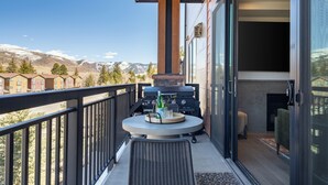 Ein Balkon mit Grill, einem runden Tisch und Flaschen sowie Blick auf Berge.