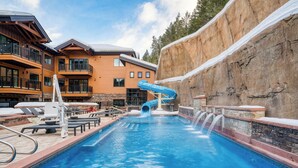 Ein Schwimmbecken mit Wasserrutsche, Liegestühlen und einem Gebäude mit Balkonen.