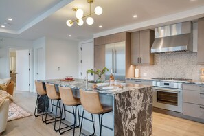 Een moderne keuken met een centraal eiland, barstoelen, roestvrijstalen apparatuur en een backsplash met een herringbone-patroon.