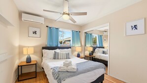 Een hotelkamer met een bed, nachtkastjes, een plafondventilator, een airconditioning en een raam met gordijnen, plus een spiegel.