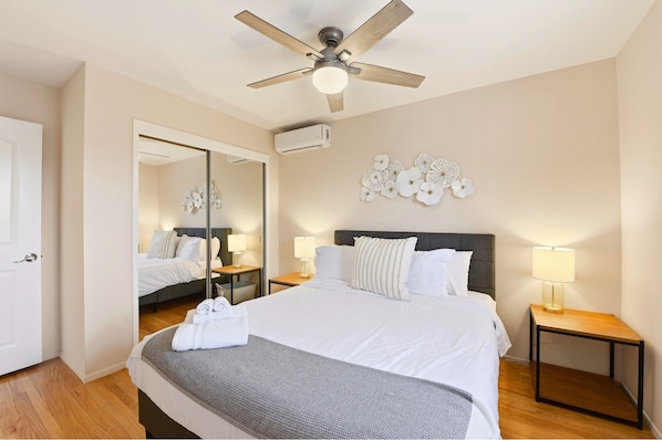 Una habitación de hotel con cama, mesitas de noche, ventilador de techo, espejo y decoración en la pared.