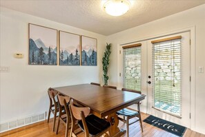 A dining area with a wooden table and chairs, a door with a window, and a wall-mounted artwork.