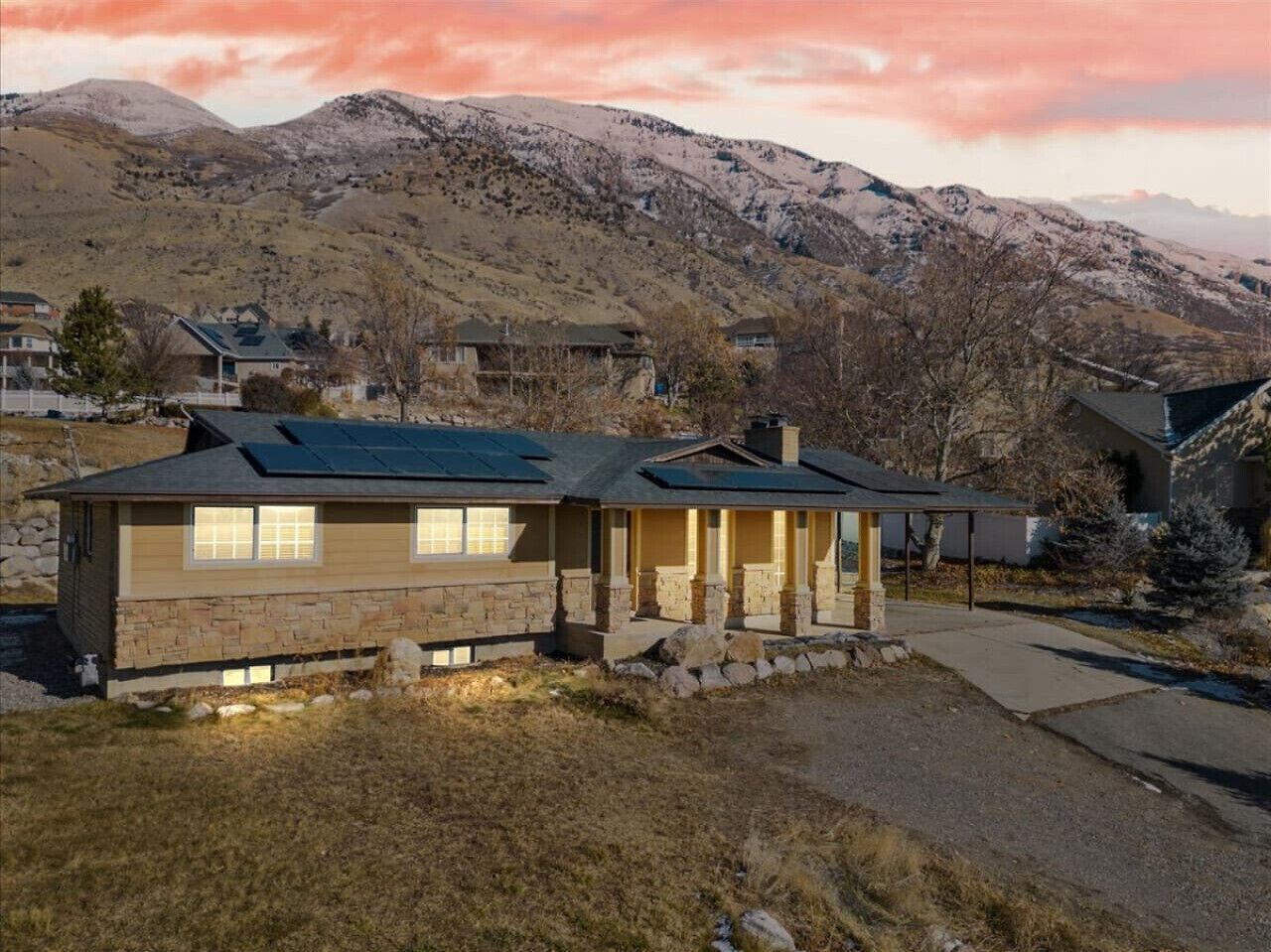 A two-story house with a stone facade, a covered porch, and a mountain backdrop.