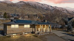 A two-story house with a stone facade, a covered porch, and a mountain backdrop. - Canyon Ridge Getaway | Arcade| View | Free Massage* (Cedar Hills)